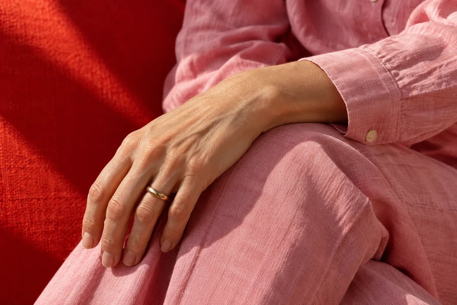 A hand resting on pink linen in sunlight.